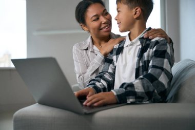 Caring mother helps her son in online learning, they sit together on the couch with a laptop
