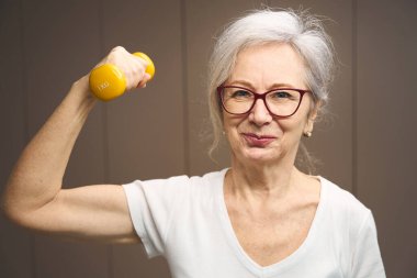 Cheerful pensioner works out with dumbbells to maintain health, she is in a good mood