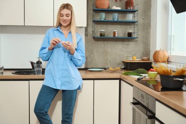 Pleased female person standing in kitchen and taking capsule out of clear plastic medicine storage box