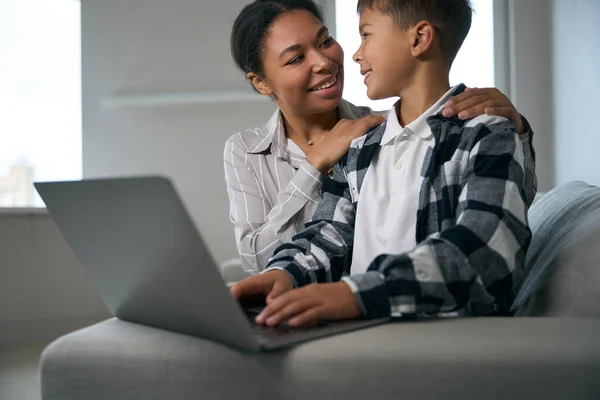 아이를 엄마는 아이가 온라인 학습을 수있도록 줍니다 소파에 앉아서 랩탑을 — 스톡 사진