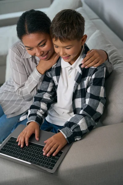 아이는 노트북으로 타자를 엄마는 온라인 학습을 소파에 — 스톡 사진