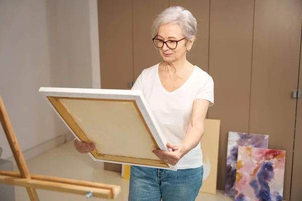 笑顔の高齢者の女性は彼女の手のストレッチャーにキャンバスを保持し クローゼットによって完成した絵画 — ストック写真