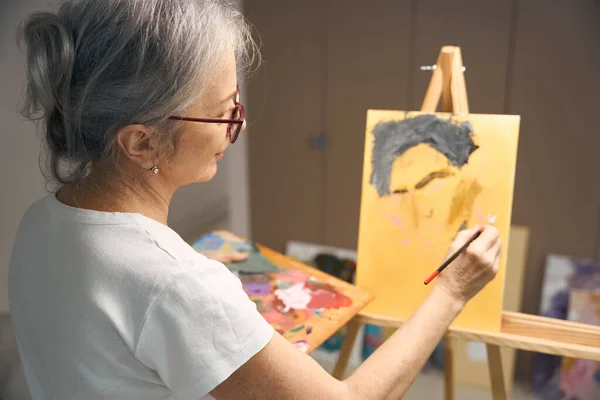 安详的老妇人用绘画和刷子画了一幅肖像 描绘了她的业余爱好 — 图库照片