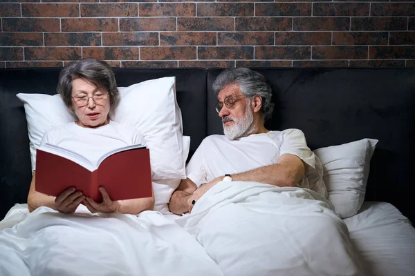 Yaşlı Çift Yatak Odasında Yatıyor Karısı Uyumadan Önce Kocasına Kitap — Stok fotoğraf