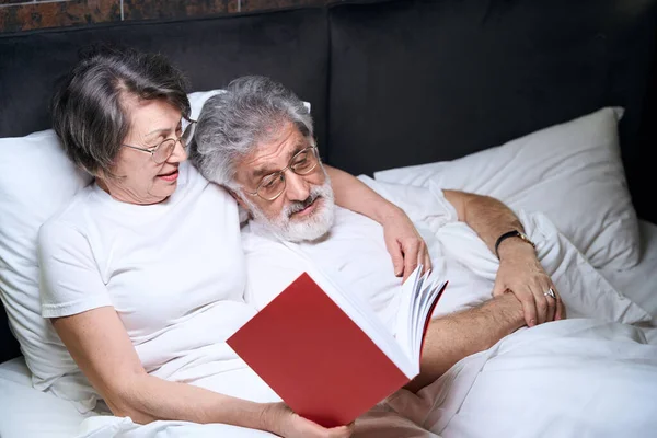 Пожилая Женщина Мужчина Лежат Кровати Спальне Жена Читает Книгу Мужу — стоковое фото