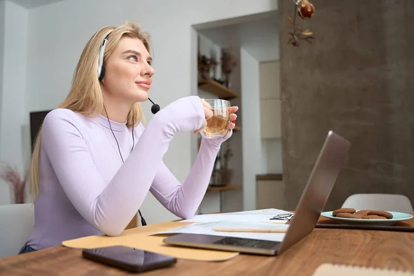 Pensive Woman Headset Holding Cup Herbal Tea While Sitting Laptop — ストック写真