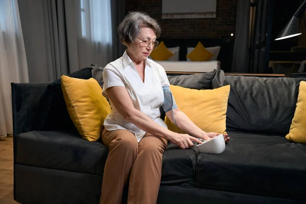 Lonely Elderly Woman Sits Comfortable Sofa Measures Her Blood Pressure — Stock Photo, Image