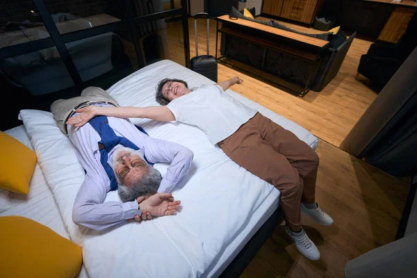 Yoldan Yorgun Ama Mutlu Yaşlı Gezginler Bir Otel Yatağında Dinleniyor — Stok fotoğraf