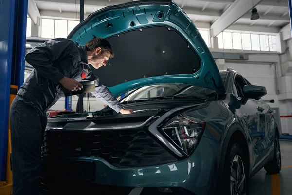 stock image Mechanic in protective clothes standing in tire fitting near car and looking under open hood