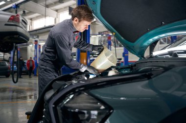 Koruyucu elbiseli bir adam lastik montajı yapıyor ve motor yağı tutuyor.