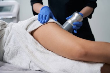 Kuaförde kanepede uzanan genç bayan, koruyucu eldivenli kozmetik uzmanı, bacak kaldırma hareketi yapıyor.