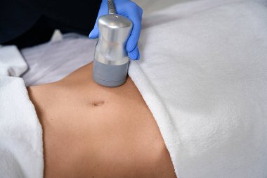 Kuaförde kanepede uzanan kadın koruyucu eldivenli kozmetolog karın röntgeni için RF kaldırıyor.