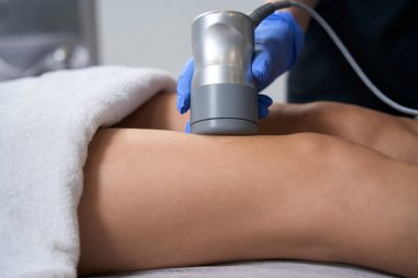 Kuaförde kanepede uzanan kadın, koruyucu eldivenli doktor bacak kaldırma hareketi yapıyor.