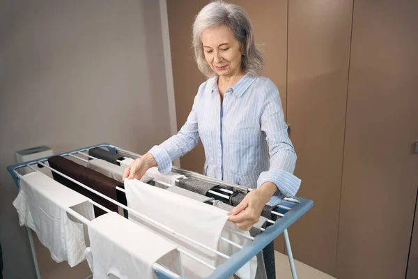 スレンダーなお年寄りの女性は 洗濯乾燥機で均等に掛けます カジュアルな服の女性 — ストック写真