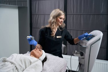 Kuaförde kanepede uzanan güzel bir kadın koruyucu eldivenli kozmetik uzmanı yüz gerdirme ameliyatı yapıyor.