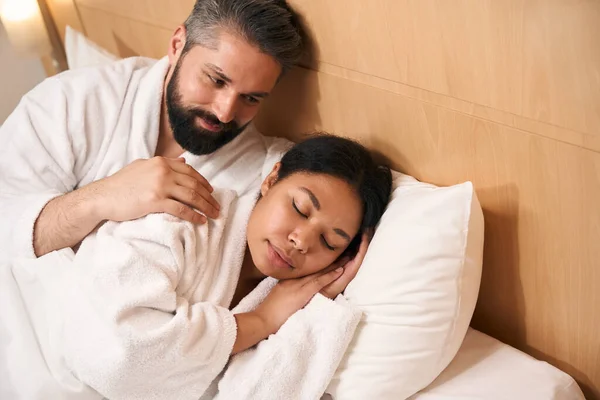 笑笑快乐的男人在床上爱慕他年轻熟睡的女伴 — 图库照片