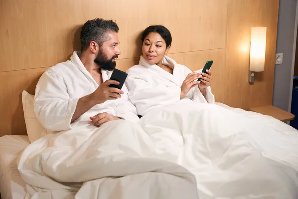 침대에 친구에게 스마트폰으로 무엇인가를보여 젊은이는 즐거워 — 스톡 사진