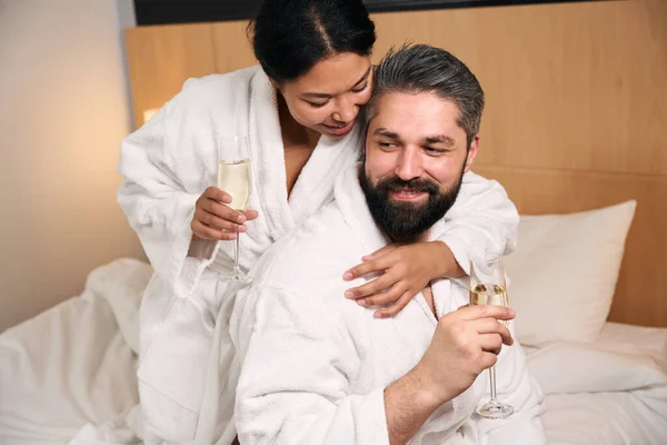 Vrolijke Vrouw Met Glas Champagne Knuffelen Haar Tevreden Metgezel Bed — Stockfoto