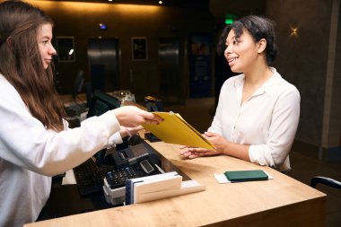 Genç otel müdürü, resepsiyonda neşeli turistlere kayıt formu gösteriyor.