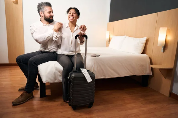 带着行李的快乐女士和她快乐的伴侣坐在豪华套间的床上 — 图库照片