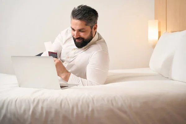 携帯電話で仕事をしながらホテルの部屋に寝そべっている幸せなビジネスマンの笑顔 — ストック写真