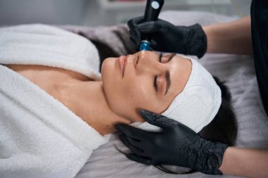 Koruyucu eldivenli kozmetik uzmanı güzel bir kadının yanında oturuyor ve kuaförde hidroterapi ameliyatı yapıyor.