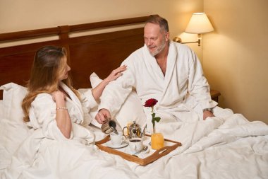 Güzel bir kadın kocasının omzuna hafifçe dokunur, otel odasında bir çift kahve içer.