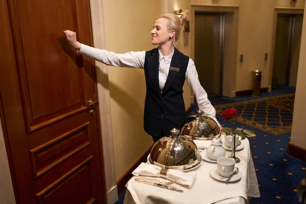ホテルの部屋のドアをノックする制服を着たウエートレスは ロマンチックな食事のために食べ物を配達しました — ストック写真