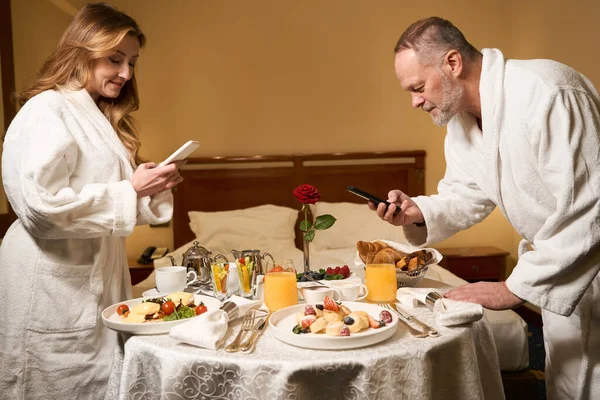 男と女はホテルの部屋で朝食の写真を撮ってる結婚記念日を祝ってる — ストック写真