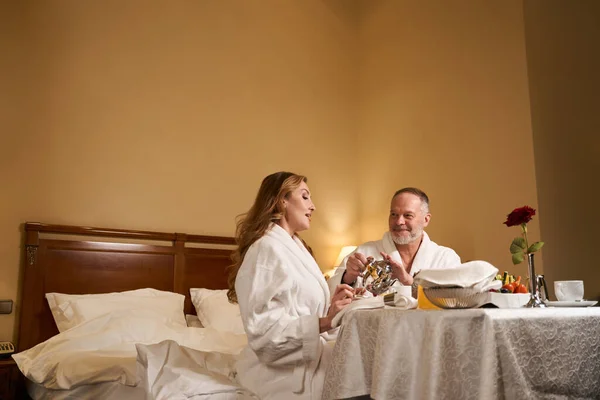 男性と女性はホテルの部屋でベッドで朝食を食べています結婚記念日を祝っています — ストック写真