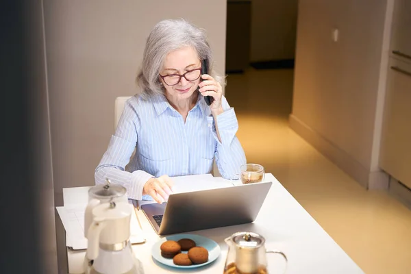 Lächelnde Ältere Dame Kommuniziert Ruhig Telefon Sie Sitzt Mit Laptop — Stockfoto