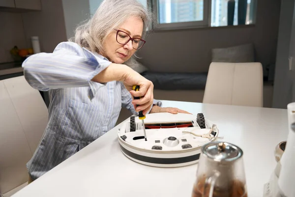 Geavanceerde Oudere Vrouw Met Bril Repareert Een Robot Stofzuiger Gelegen — Stockfoto