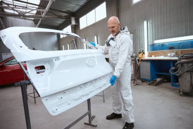 Boyama ustası arabanın bir parçasıyla çalışıyor. Adam büyük bir oto tamirhanesinde.