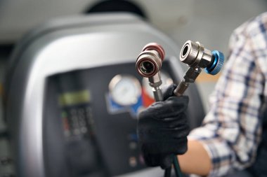 Usta, araba kliması için özel bir sifon sisteminin hortumlarını elinde tutuyor. Koruyucu eldivenli bir tamirci.