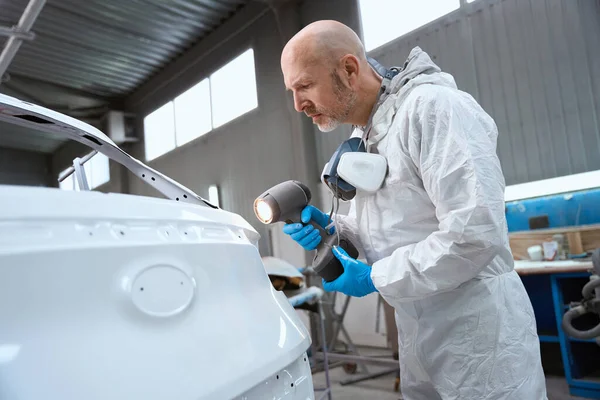 Painter uses a special flashlight to select paint for a car, a man uses a respirator