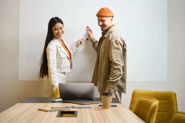 Uśmiechnięci Pracownicy Firmy Wskazujący Markery Tablicę Patrząc Ekran Laptopa — Zdjęcie stockowe