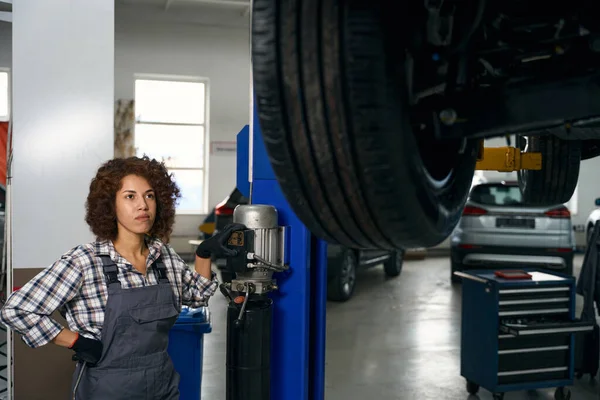 Młody Mechanik Ubraniach Roboczych Podnosi Samochód Specjalnej Windzie Kobieta Pracuje — Zdjęcie stockowe