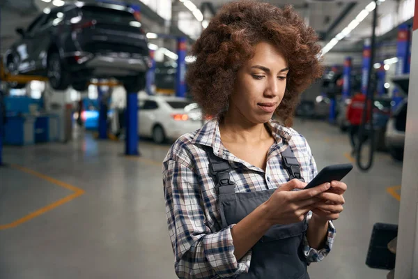 現代の自動車修理店の若い従業員は 携帯電話 作業服の修理の女性のボタンを押してください — ストック写真
