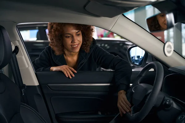 かわいい多人種の女性は 新しい車のインテリアを見て インテリアは暗い色で作られています — ストック写真