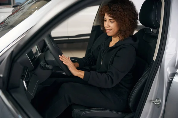 かわいい笑顔の女性が新しい車のインテリアに座って インテリアは暗い色で作られています — ストック写真