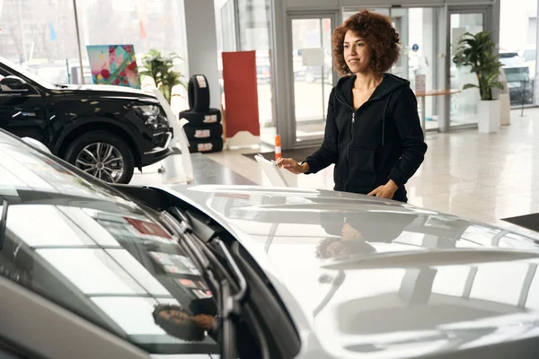 笑顔多人種の女性が新しい車の近くに立って 車は専門のサロンで販売されています — ストック写真