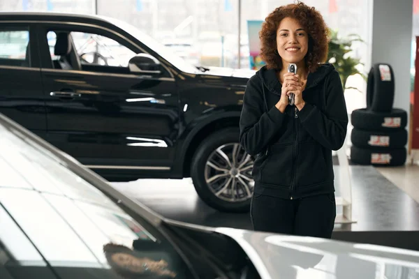 車のディーラーの喜びの顧客は 彼女の手の中に新しい車への鍵を保持します 快適なカジュアル服の女性 — ストック写真