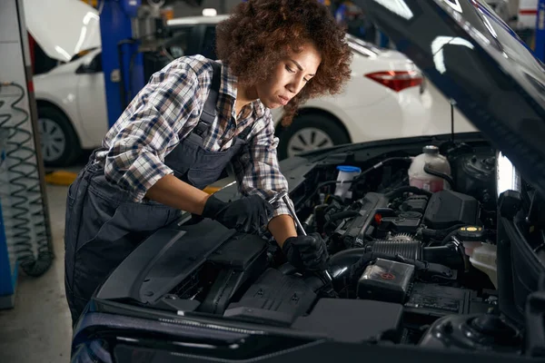 Multiracial auto repair shop employee in protective gloves repairs car engine, woman in work clothes