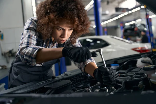 妇女汽车修理工在一家现代汽车修理店里修理汽车 主人在汽车的车篷下鬼混 — 图库照片
