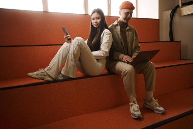 Arkadaşı taşınabilir bilgisayarda çalışırken genç bir kadın cep telefonuyla zaman geçiriyor.