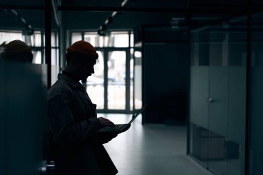 Taşınabilir bilgisayarda yazarken duvara yaslanan konsantre şirket çalışanlarının yan görünümü