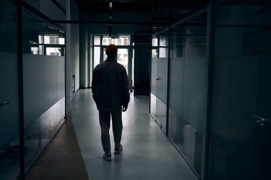 Ofis binasındaki karanlık koridorda yürüyen şirket çalışanlarının arka görüntüsü