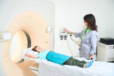 Bayan doktor küçük hastayı klinikteki CT kamerasına gönderiyor.