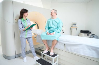 Mutlu erkek hasta, kadın doktora bakarken MRI testinden önce bir anket tamamlıyor.