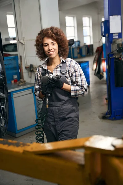 Uśmiechnięta Wielorasowa Kobieta Trzymająca Śrubokręt Rękach Pracuje Warsztacie Samochodowym — Zdjęcie stockowe